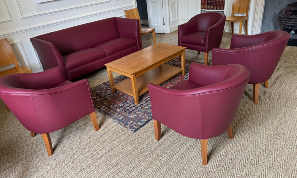 A 2-seater sofa and 4 tub chairs in real burghundy leather arranged around a coffee table.