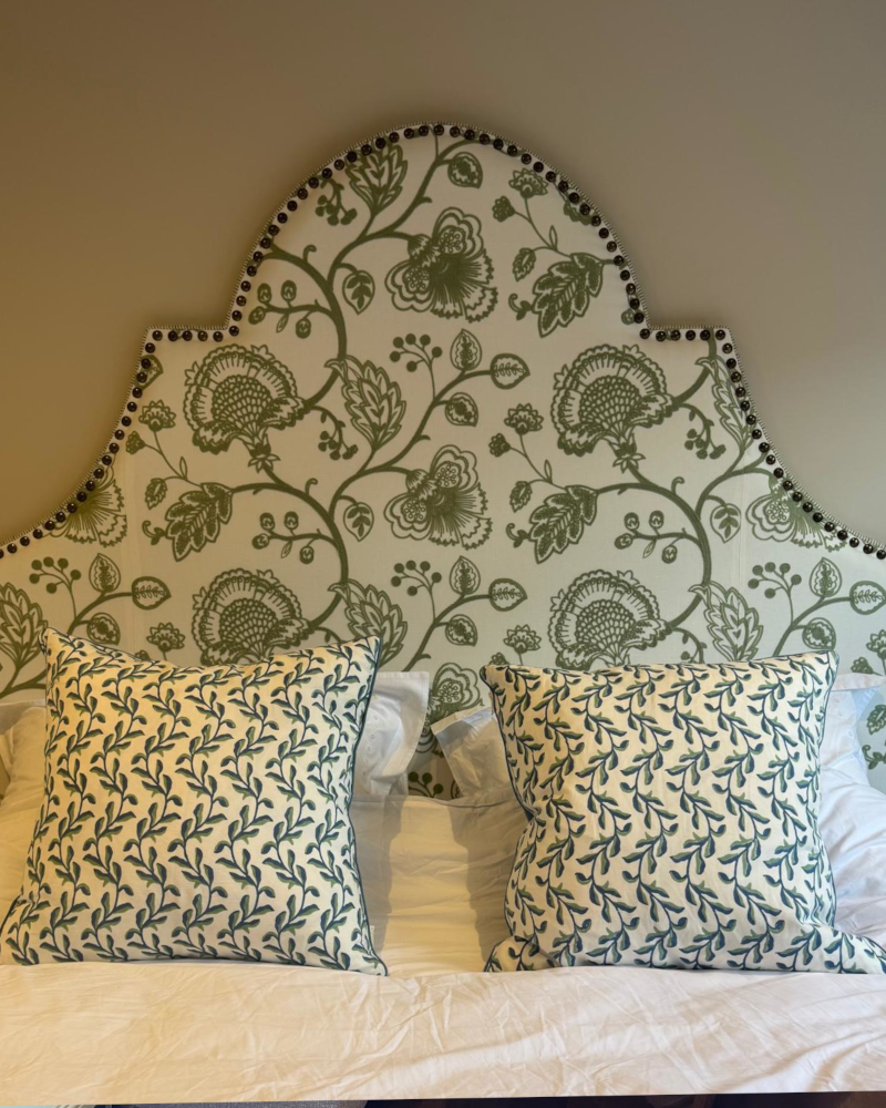 A shaped headboard with big antique brass studs and a white and green embroidered plant fabric.